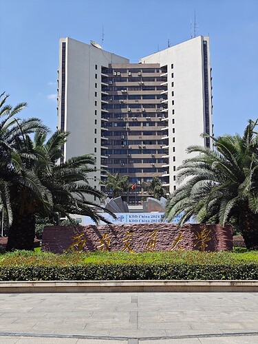 The image shows a large, multi-story building with a sign and palm trees in front of it. (由 AI 生成标题)