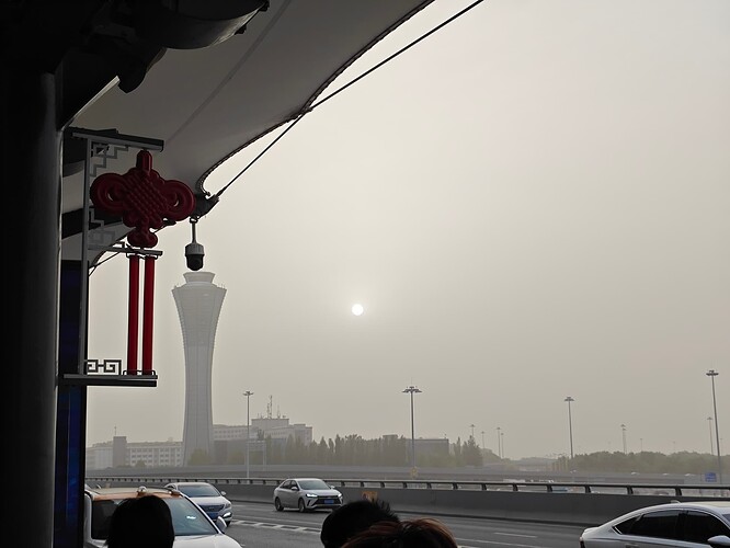 The photograph shows a hazy cityscape with a busy highway in the foreground, a large tower in the background, and a red ornament hanging from a roof. (由 AI 生成标题)
