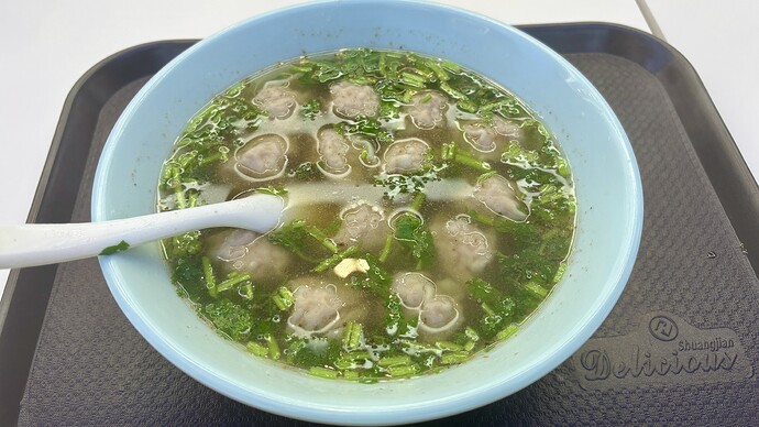 这是一碗盛在蓝色碗里的，撒有绿色蔬菜和肉丸的汤。 (由 AI 生成标题)