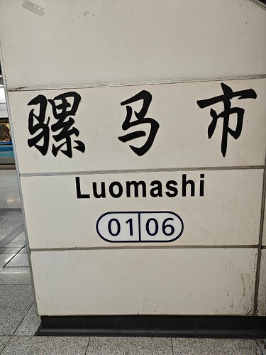 The image shows a sign with Chinese characters and English text, reading "Luomashi" and "01 06". (由 AI 生成标题)