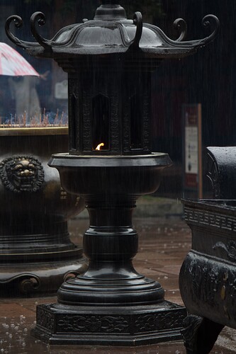 The image depicts a rainy scene featuring an ornate, black, pagoda-style lantern with a small flame burning inside, situated on a wet stone floor amidst other similar structures. (由 AI 生成标题)